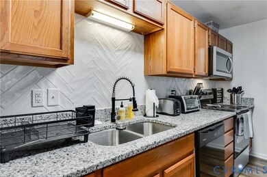 Kitchen featuring decorative backsplash, black appliances, light stone counters, and brown cabinets