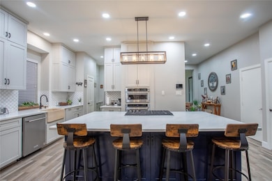 Kitchen with decorative backsplash, light wood-type flooring, decorative light fixtures, light stone countertops, and a kitchen bar