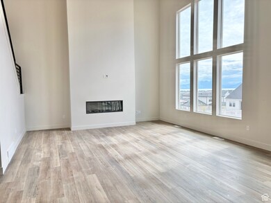 Unfurnished living room with a glass covered fireplace, light wood-style flooring, and a towering ceiling