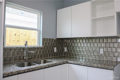 Kitchen featuring white cabinets, backsplash, sink, and dark stone counters