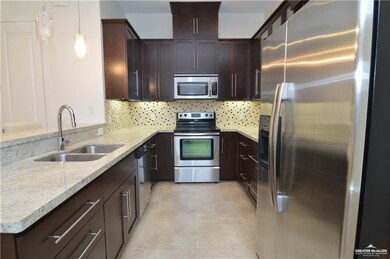 Kitchen with tasteful backsplash, light stone counters, hanging light fixtures, sink, and stainless steel appliances