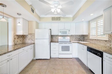 Kitchen with ornamental molding, white appliances, white cabinetry, backsplash, and light stone countertops