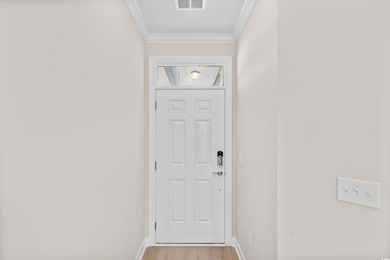 Entryway with baseboards, visible vents, light wood-style flooring, and ornamental molding