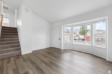 Empty room featuring dark wood-style floors, vaulted ceiling, stairs, and a mountain view