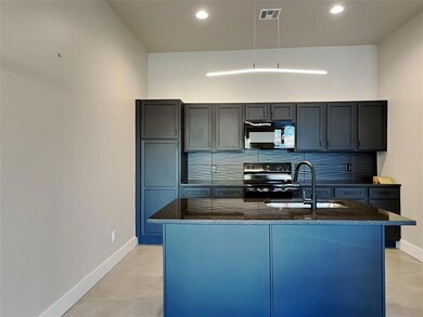 Kitchen with dark stone counters, sink, decorative backsplash, an island with sink, and black appliances