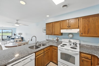 Kitchen featuring white appliances, under cabinet range hood, a peninsula, brown cabinetry, and stone countertops