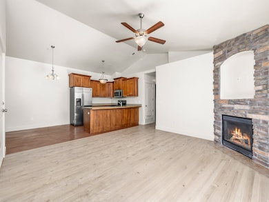 Kitchen featuring open floor plan, brown cabinets, hanging light fixtures, light wood finished floors, and vaulted ceiling