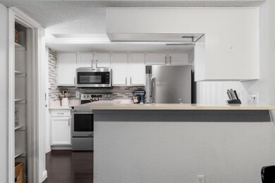 Kitchen with white cabinetry, appliances with stainless steel finishes, dark wood-style floors, tasteful backsplash, and a textured ceiling