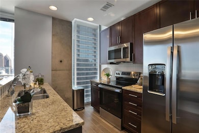 Kitchen featuring appliances with stainless steel finishes, dark wood-type flooring, dark brown cabinetry, light stone countertops, and backsplash