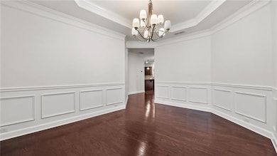 Unfurnished dining area with a chandelier, a tray ceiling, crown molding, wood finished floors, and wainscoting