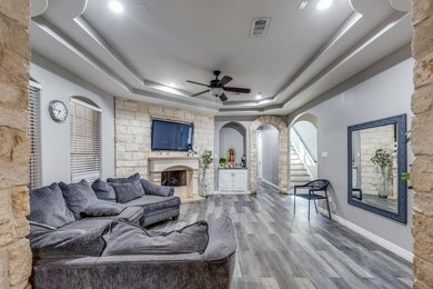 Living area featuring arched walkways, wood finished floors, a fireplace, ceiling fan, and a tray ceiling