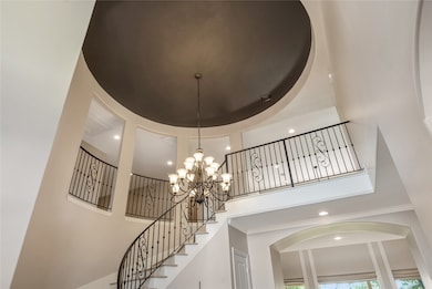 A breathtaking view of the foyer highlights the dramatic domed ceiling, statement chandelier, and beautifully crafted iron railing. This striking architectural moment sets an upscale tone the moment you step inside.