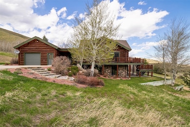 Log-style house with stone siding, a wooden deck, a garage, a front yard, and log siding