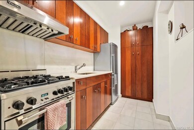 Kitchen with stainless steel appliances, exhaust hood, brown cabinets, light tile patterned floors, and light stone counters