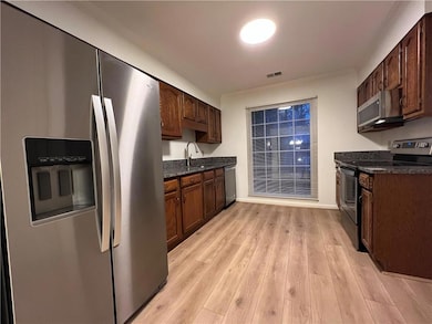 Kitchen featuring stainless steel appliances, light wood finished floors, dark stone countertops, dark brown cabinets, and crown molding