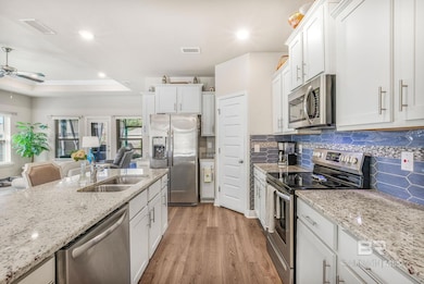 Kitchen featuring stainless steel appliances, white cabinetry, open floor plan, light stone counters, and recessed lighting