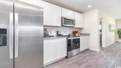 Kitchen featuring stainless steel appliances, white cabinetry, light wood finished floors, light stone countertops, and recessed lighting