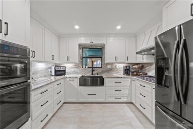 Kitchen featuring appliances with stainless steel finishes, white cabinetry, tasteful backsplash, light stone counters, and recessed lighting