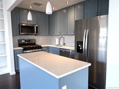 Kitchen featuring stainless steel appliances, tasteful backsplash, a kitchen island, decorative light fixtures, and dark wood-type flooring