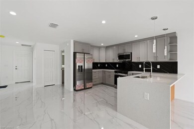 Kitchen featuring gray cabinetry, open shelves, backsplash, light marble finish floors, and appliances with stainless steel finishes