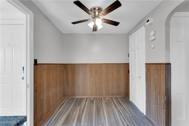 Unfurnished room with arched walkways, a wainscoted wall, wooden walls, wood finished floors, and a ceiling fan