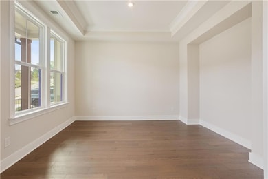 Empty room with ornamental molding, dark wood-type flooring, a tray ceiling, baseboards, and recessed lighting