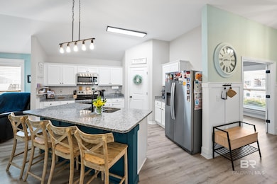 Kitchen featuring healthy amount of natural light, stainless steel appliances, white cabinetry, light stone countertops, and lofted ceiling