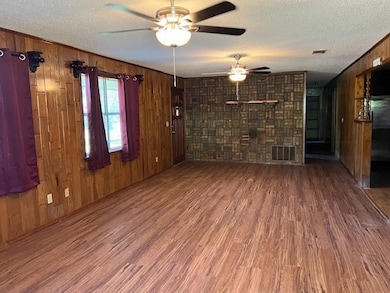 Unfurnished living room with wood walls, ceiling fan, wood-type flooring, and a textured ceiling