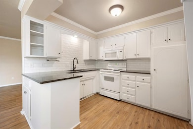 Kitchen featuring backsplash, ornamental molding, white appliances, open shelves, and white cabinetry