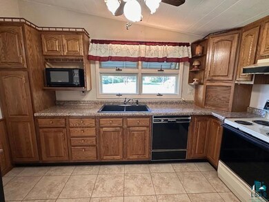 Kitchen with black appliances, a sink, lofted ceiling, and brown cabinetry