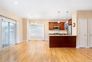 Kitchen with backsplash, hanging light fixtures, brown cabinets, recessed lighting, and light wood-type flooring