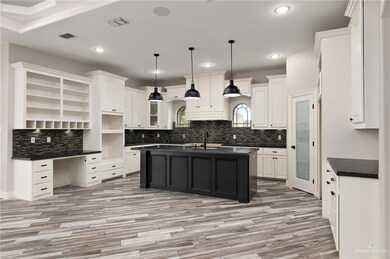 Kitchen with white cabinets, light wood-type flooring, a kitchen island with sink, and hanging light fixtures