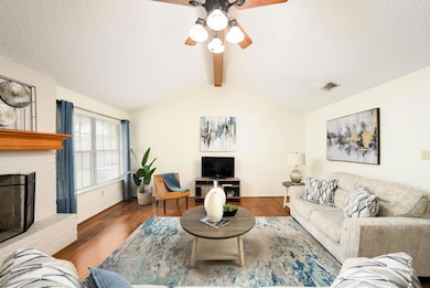 Living room with wood finished floors, a textured ceiling, ceiling fan, and a fireplace