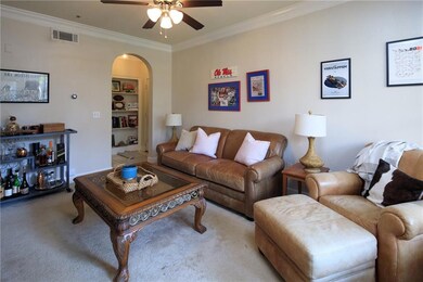 Living area featuring arched walkways, crown molding, carpet, a ceiling fan, and built in shelves