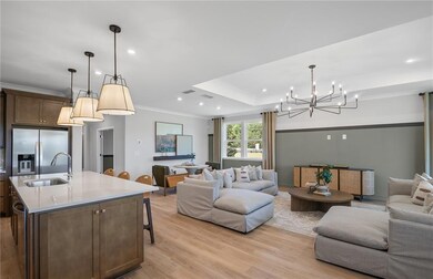 Model RepresentationLiving room with light LVP finished floors, a chandelier, recessed lighting, and crown molding.