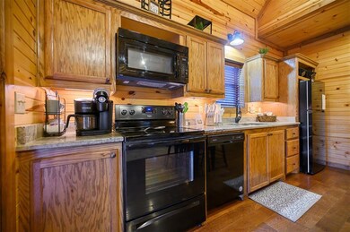 Kitchen featuring vaulted ceiling, wooden walls, sink, black appliances, and dark wood-type flooring