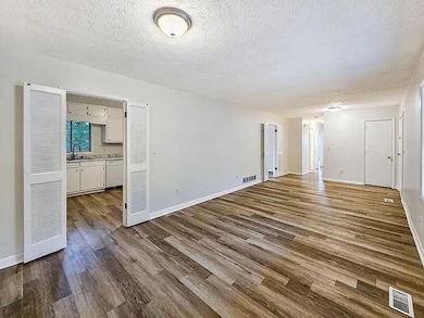 Kitchen with white appliances, under cabinet range hood, dark wood-style floors, white cabinets, and a textured ceiling