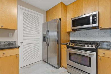 Kitchen with stainless steel appliances, light marble finish flooring, backsplash, and dark stone counters