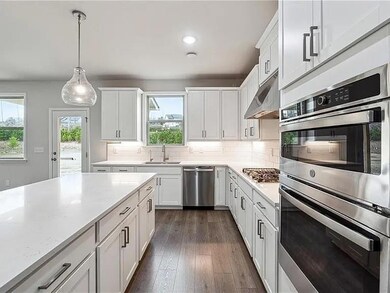 Kitchen featuring stainless steel appliances, under cabinet range hood, light countertops, white cabinets, and dark wood-style floors