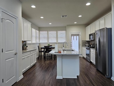 Kitchen with stainless steel appliances, backsplash, dark wood-style flooring, white cabinetry, and recessed lighting