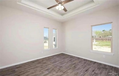 Unfurnished room featuring a tray ceiling, dark wood-style flooring, baseboards, ceiling fan, and crown molding