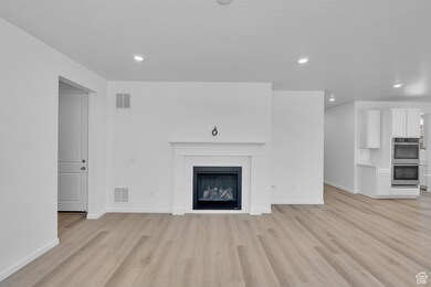 Unfurnished living room featuring light wood-type flooring, a glass covered fireplace, and recessed lighting
