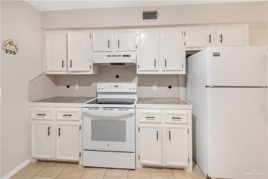 Kitchen featuring white appliances, white cabinets, light countertops, and under cabinet range hood