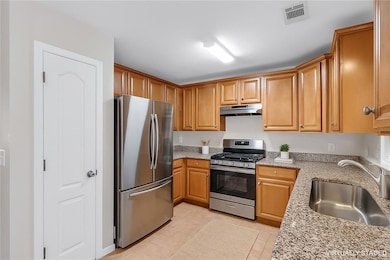 Kitchen with stainless steel appliances, under cabinet range hood, light stone countertops, and light tile patterned floors