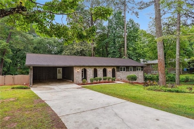 Ranch-style home featuring concrete driveway, brick siding, an attached carport, a shingled roof, and view of wooded area