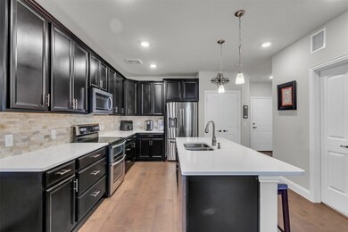 Kitchen featuring a center island with sink, stainless steel appliances, pendant lighting, decorative backsplash, and sink