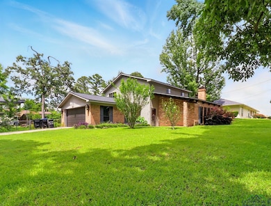 View of front of home featuring brick siding, a garage, a front yard, and a chimney