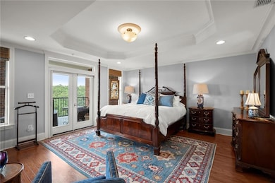 Bedroom with a tray ceiling, access to exterior, wood finished floors, ornamental molding, and french doors