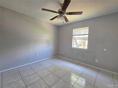 Tiled empty room with a ceiling fan, baseboards, and a textured ceiling