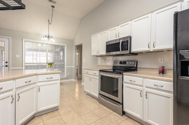 Kitchen with stainless steel appliances, light countertops, tasteful backsplash, vaulted ceiling, and white cabinets